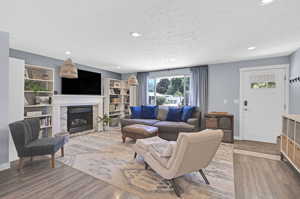 Living room with a textured ceiling, a fireplace, hardwood / wood-style flooring, and built in shelves