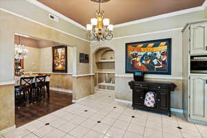 Tiled dining area featuring built in shelves, crown molding, and an inviting chandelier