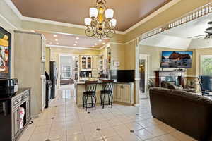 Kitchen with light tile patterned flooring, ceiling fan with notable chandelier, a breakfast bar, stainless steel refrigerator, and kitchen peninsula