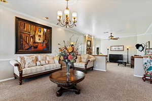 Carpeted living room featuring ceiling fan with notable chandelier and ornamental molding