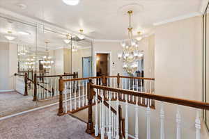 Hallway featuring carpet flooring, crown molding, and a chandelier