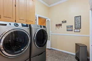 Washroom featuring crown molding, tile patterned floors, washer and dryer, and cabinets