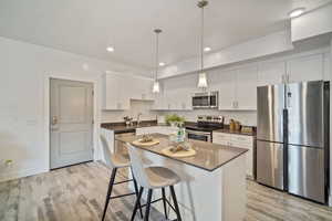 Kitchen with sink, appliances with stainless steel finishes, light wood-type flooring, and white cabinets