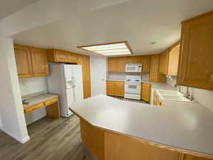 Kitchen with sink, light hardwood / wood-style flooring, kitchen peninsula, and white appliances