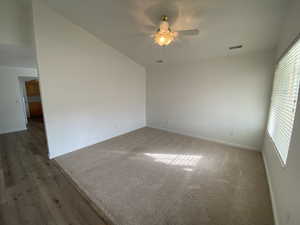 Spare room featuring dark colored carpet, ceiling fan, and vaulted ceiling