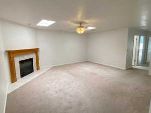 Unfurnished living room with ceiling fan, a skylight, and light colored carpet