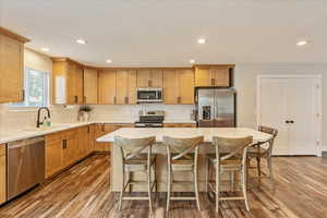 Kitchen with sink, appliances with stainless steel finishes, hardwood / wood-style flooring, and a center island