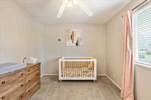 Bedroom with a crib, carpet, multiple windows, and ceiling fan