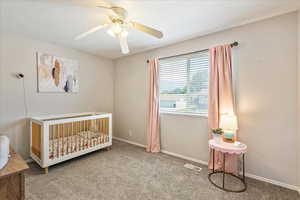 Bedroom with a crib, carpet, and ceiling fan