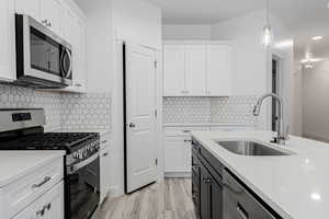 Kitchen featuring white cabinets, sink, hanging light fixtures, light hardwood / wood-style flooring, and stainless steel appliances