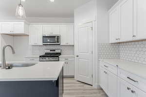 Kitchen featuring sink, white cabinets, hanging light fixtures, and appliances with stainless steel finishes