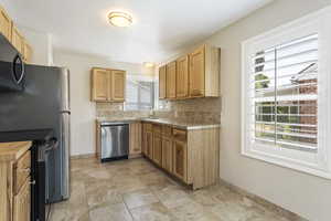 Kitchen with decorative backsplash, sink, light stone counters, appliances with stainless steel finishes, and light tile patterned floors