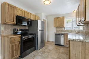 Kitchen featuring appliances with stainless steel finishes, sink, light stone counters, decorative backsplash, and light tile patterned flooring