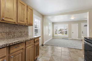 Kitchen with light stone counters, electric stove, light tile patterned floors, and backsplash