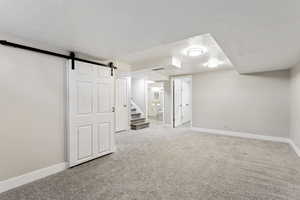 Basement featuring carpet floors, a textured ceiling, and a barn door