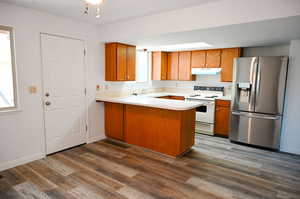 Kitchen featuring white electric range, kitchen peninsula, dark hardwood / wood-style flooring, and stainless steel fridge