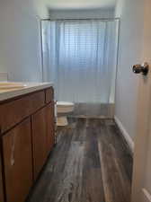 Full bathroom featuring hardwood / wood-style flooring, shower / bath combo, toilet, and vanity