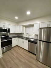 Kitchen with sink, stainless steel appliances, hardwood / wood-style floors, and white cabinets