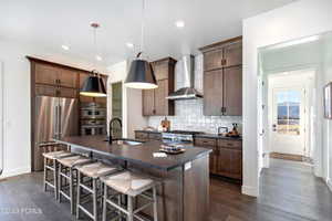 Kitchen with stainless steel appliances, dark hardwood / wood-style flooring, an island with sink, wall chimney exhaust hood, and sink