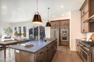 Kitchen featuring wall chimney range hood, a kitchen island with sink, appliances with stainless steel finishes, hardwood / wood-style flooring, and sink