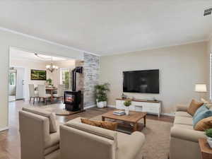 Living room featuring light hardwood / wood-style flooring, crown molding, a chandelier, and a wood stove