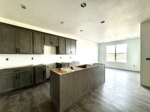 Kitchen featuring dark wood-type flooring, a center island, dark brown cabinets, and a textured ceiling