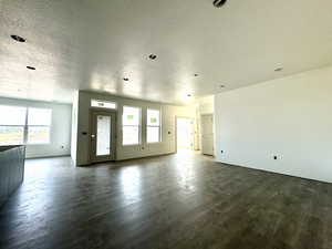 Unfurnished living room with a textured ceiling, dark hardwood / wood-style flooring, and a healthy amount of sunlight