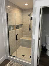 Bathroom with a shower with shower door, wood-type flooring, and toilet