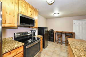 Kitchen with light stone countertops, appliances with stainless steel finishes, light tile patterned floors, and a textured ceiling