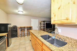 Kitchen featuring range, sink, light stone counters, light tile patterned floors, and a textured ceiling