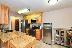 Kitchen featuring light tile patterned flooring, light stone countertops, appliances with stainless steel finishes, stacked washer and clothes dryer, and sink