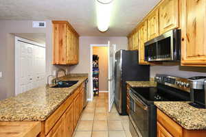 Kitchen with sink, light stone countertops, stainless steel appliances, and a textured ceiling