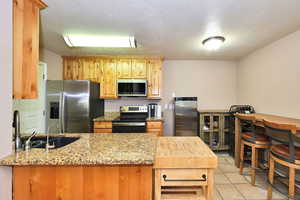 Kitchen with light tile patterned flooring, sink, light stone counters, appliances with stainless steel finishes, and a textured ceiling