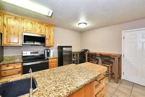 Kitchen featuring stainless steel appliances, sink, light tile patterned floors, a textured ceiling, and light stone countertops