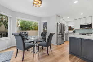 Kitchen with dining area featuring white cabinetry, stainless steel appliances, decorative backsplash, and light wood-type flooring