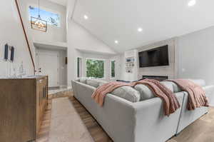 Living room with a fireplace, a notable chandelier, light wood-type flooring, and high vaulted ceiling