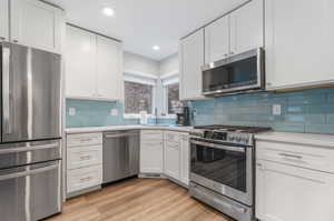 Kitchen featuring white cabinetry, backsplash, appliances with stainless steel finishes, and light wood-type flooring