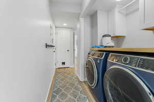 Clothes washing area with cabinets, washer and dryer, and light wood-type flooring