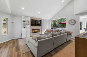 Living room featuring a large fireplace, high vaulted ceiling, plenty of natural light, and hardwood / wood-style floors