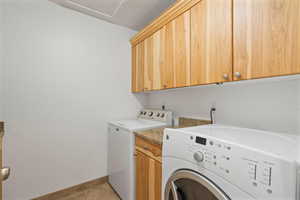 Laundry room with light tile patterned flooring, separate washer and dryer, and cabinets