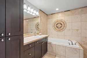 Primary ensuite with vanity, tile patterned floors, tile walls, and a relaxing tiled tub