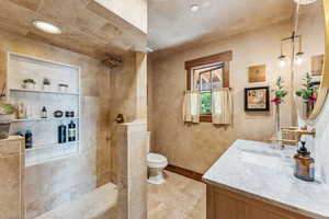 Bathroom with tile patterned floors, vanity, a tile shower, and toilet