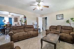 Living room with a textured ceiling, ceiling fan, and light tile patterned floors