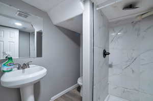 Bathroom with tiled shower, wood-type flooring, and toilet