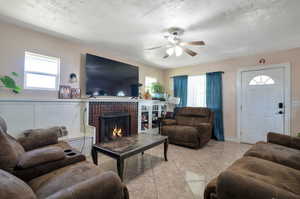 Tiled living room featuring a fireplace, a textured ceiling, and ceiling fan