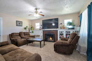 Living room featuring a textured ceiling, light tile patterned flooring, a fireplace, and ceiling fan