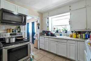 Kitchen featuring white cabinetry, stainless steel appliances, and light tile patterned flooring