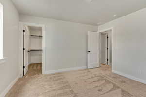 Unfurnished bedroom featuring a walk in closet, light carpet, and a closet