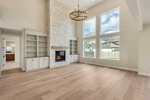 Unfurnished living room with a wealth of natural light, a fireplace, a towering ceiling, and light hardwood / wood-style floors