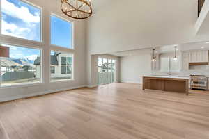 Unfurnished living room featuring plenty of natural light, a towering ceiling, and a notable chandelier